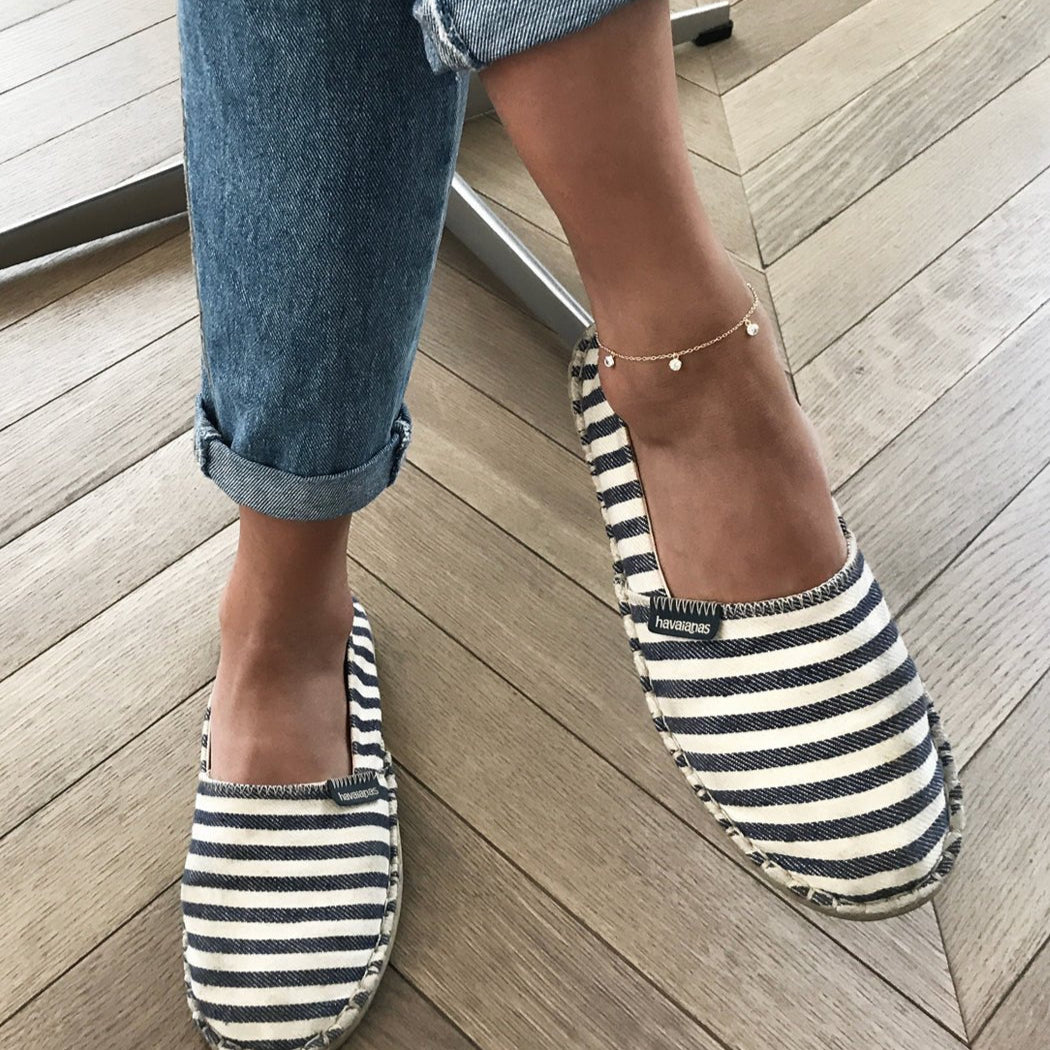 Sterling silver clear-stone dangle anklet shown on a model's ankle with striped espadrilles