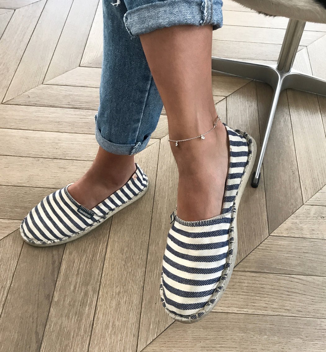 Rose gold vermeil clear-stone dangle anklet shown on a seated model's ankle with striped espadrilles