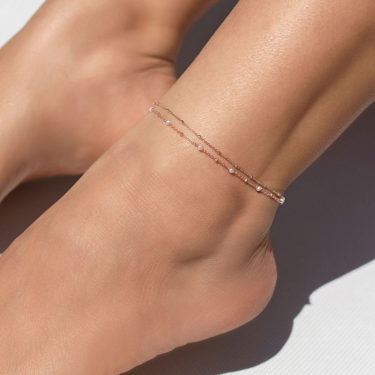 Rose gold vermeil pearl-station anklet layered with a chain, shown close up on a model's ankle