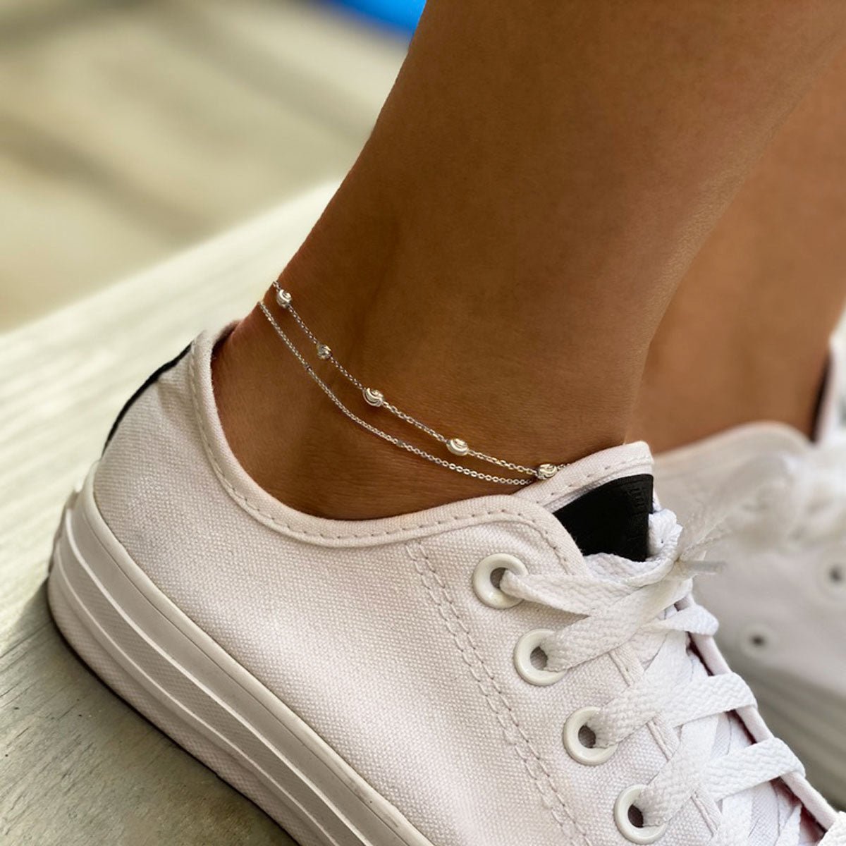 Sterling silver beaded anklet layered with a fine chain, shown on a model's ankle above a white sneaker