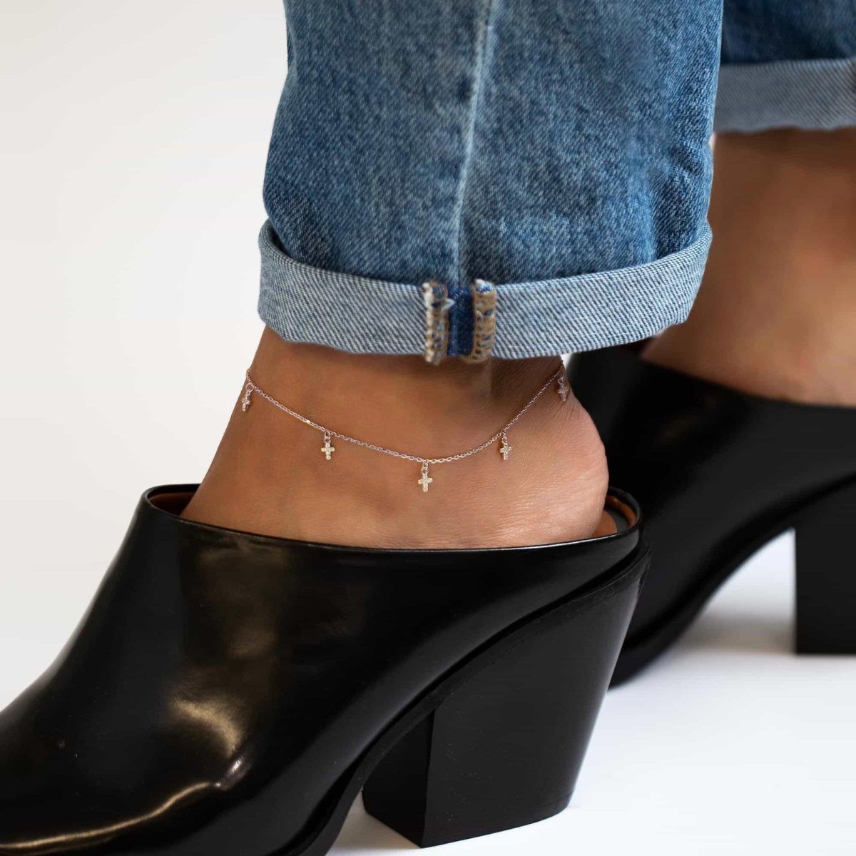 Sterling silver anklet with dangling tiny crystal-set crosses, shown on a model's ankle above a black heel