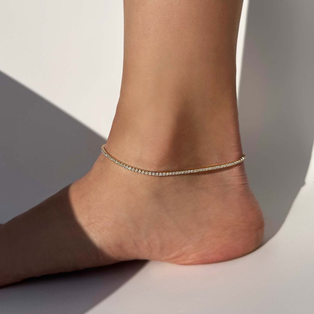 Gold vermeil anklet set with a continuous line of small crystals, worn on a bare ankle and foot