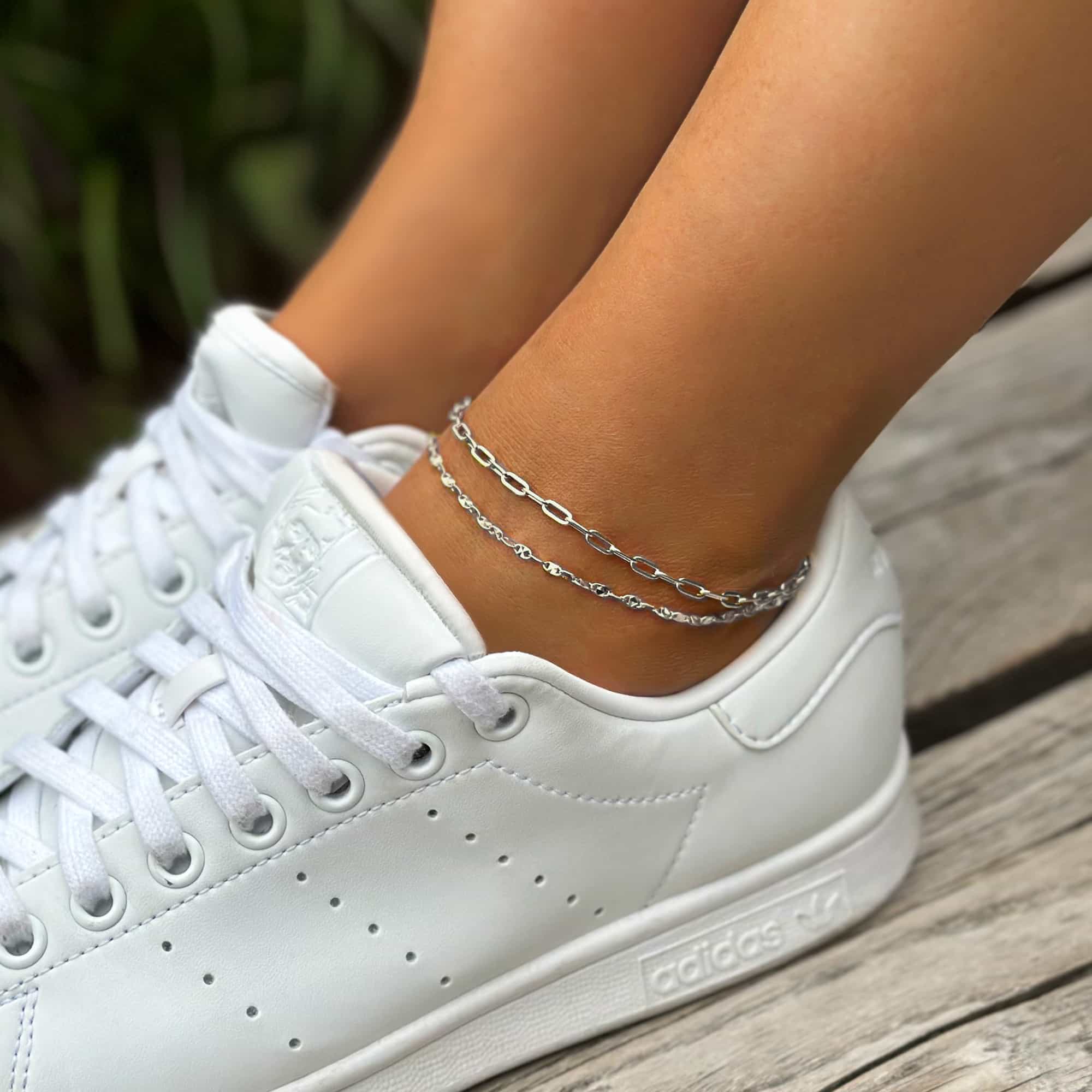 Sterling silver diamond-cut chain anklets layered on a model's ankle above a white sneaker