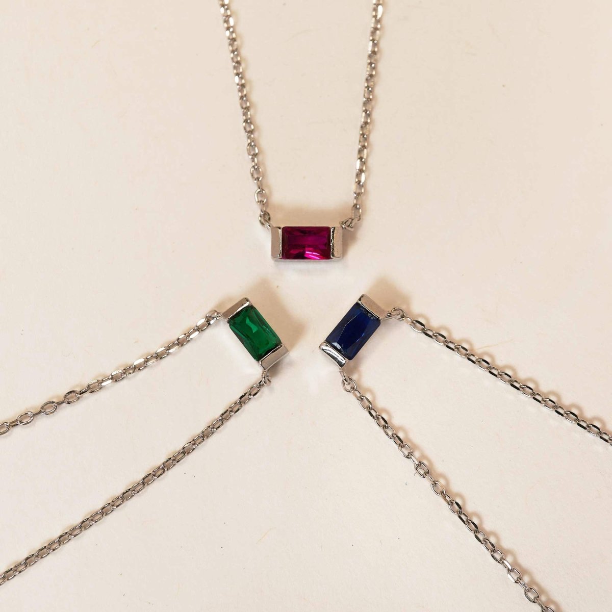 Sterling silver ruby baguette necklace among red, green and blue baguette pendants arrayed on tan