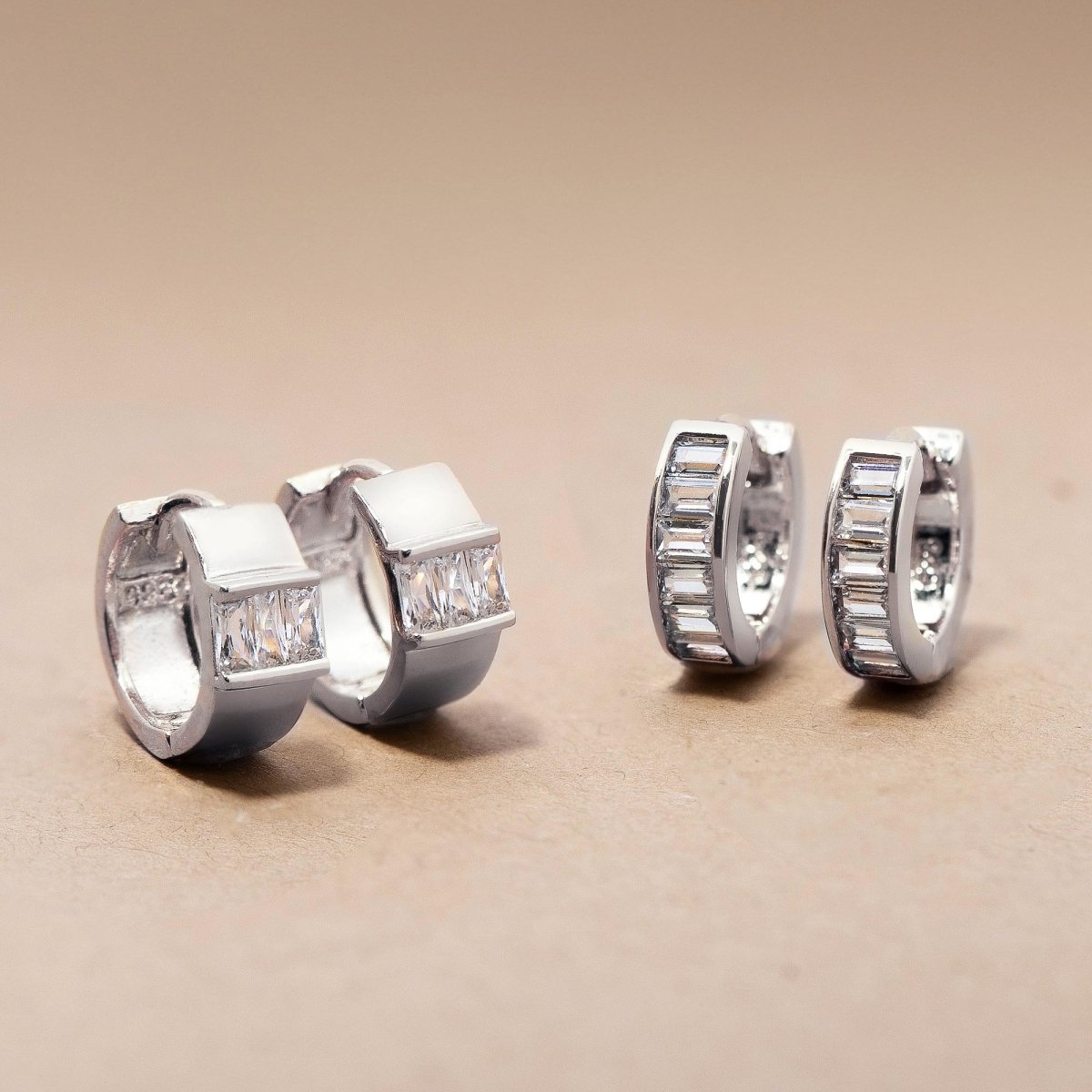 Two sterling silver baguette huggie hoops with clear stones, shown front and side on a cream background