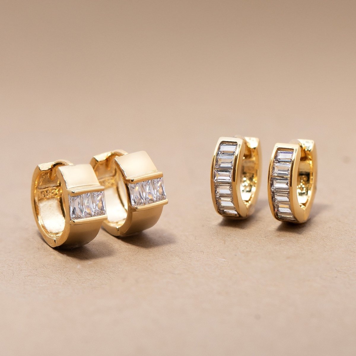 Two gold vermeil baguette huggie hoops with clear stones, shown front and side on a cream background