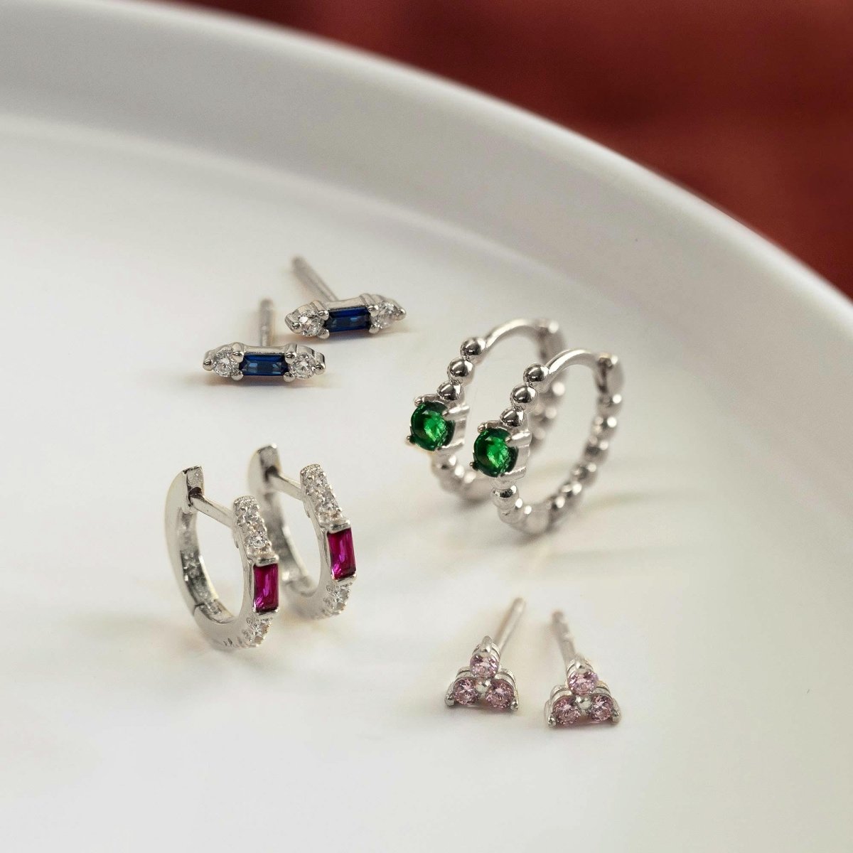 Sterling silver baguette studs with blue stones, shown with other earrings on a white dish