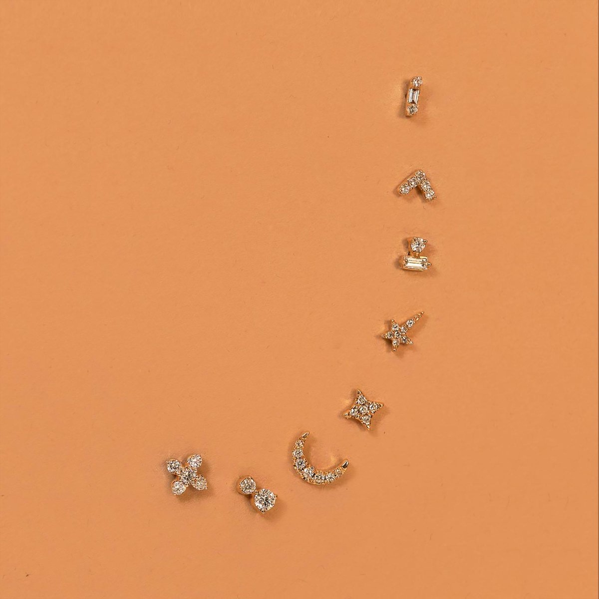14K gold diamond celestial stud earrings in star, moon and baguette shapes, on terracotta