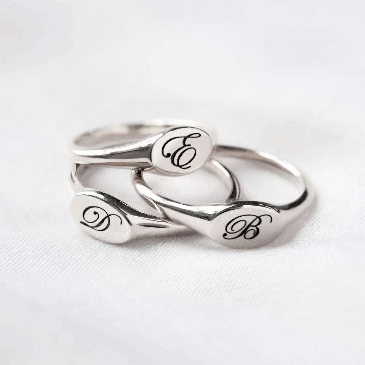 Sterling silver oval signet rings engraved with initials, stacked on soft white fabric