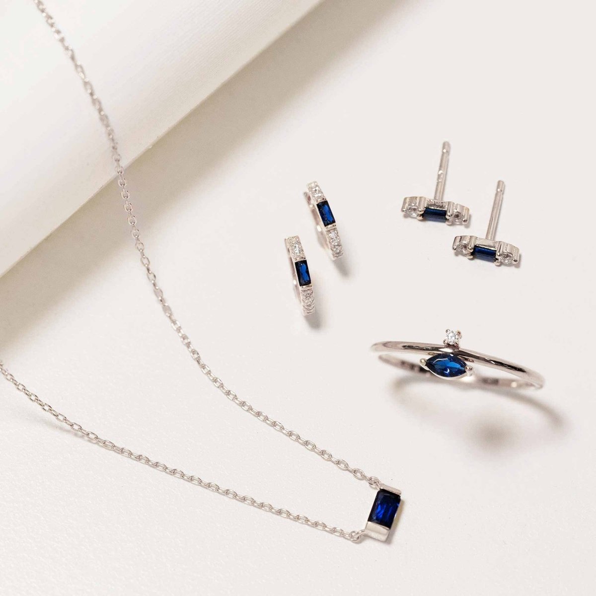 Sterling silver baguette blue sapphire necklace styled with matching hoops, studs and ring on a white background