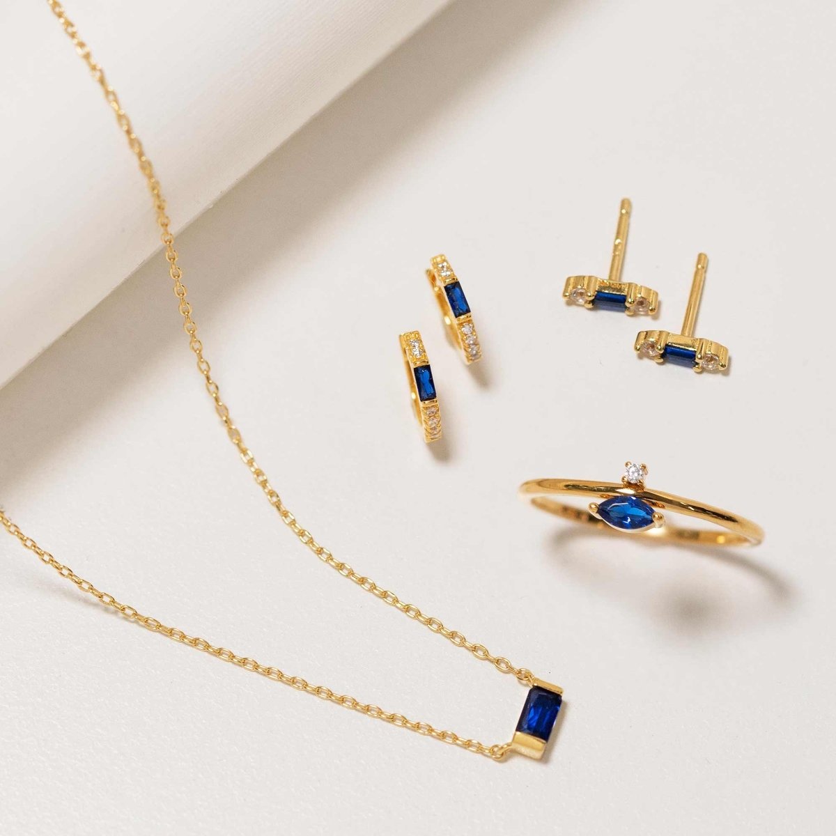 Gold vermeil baguette blue sapphire necklace styled with matching hoops, studs and ring on a white background