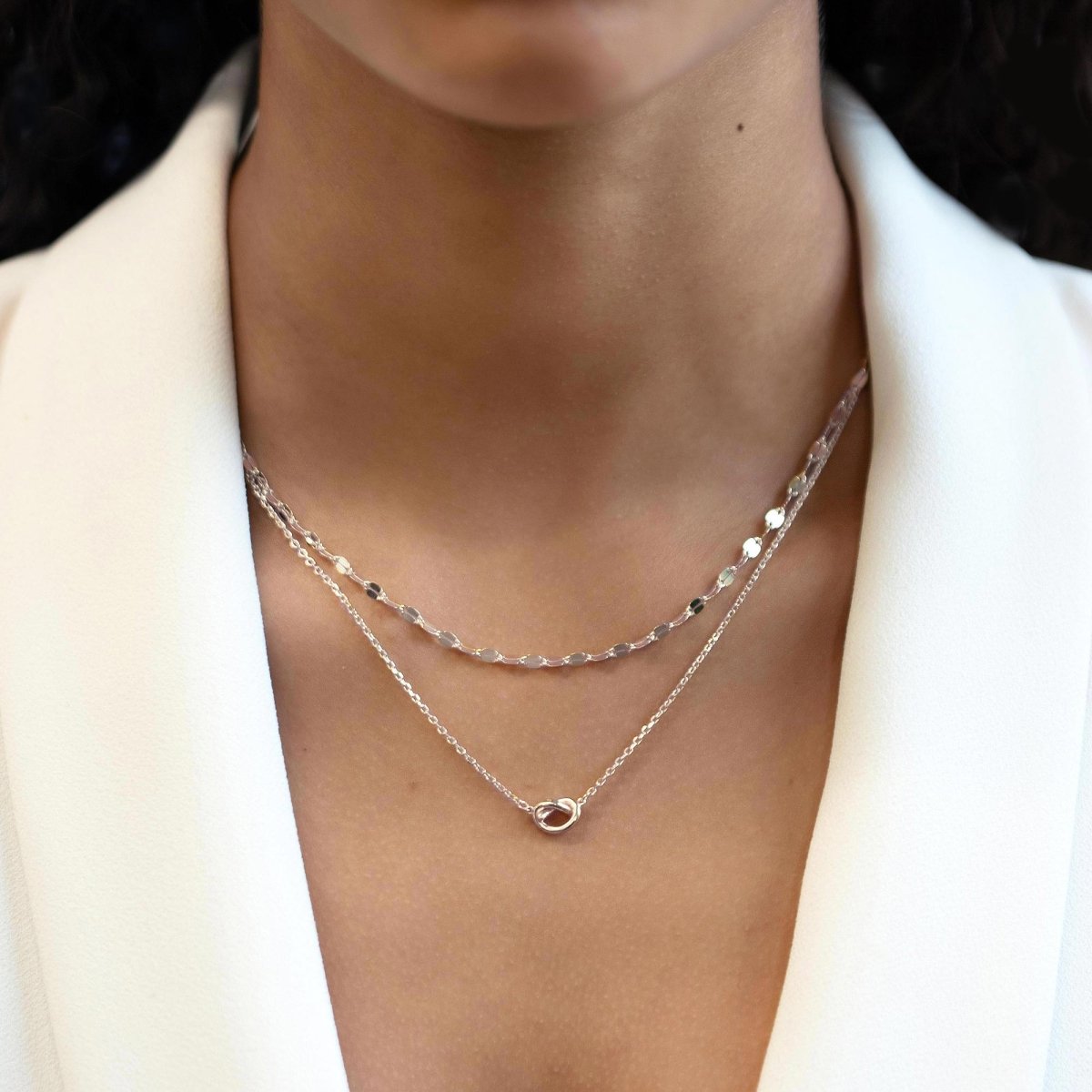 Sterling silver mirror-link chain necklace layered with a knotted-pendant chain, shown on a model's neckline