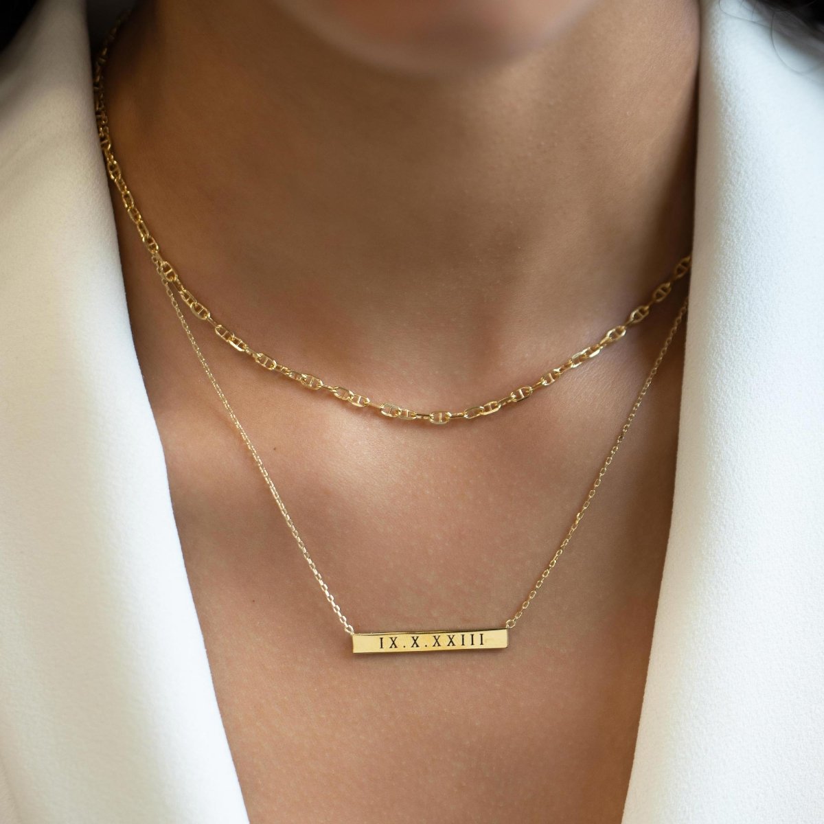 Gold vermeil bar necklace engraved with a date, layered over a chain on a model's neckline