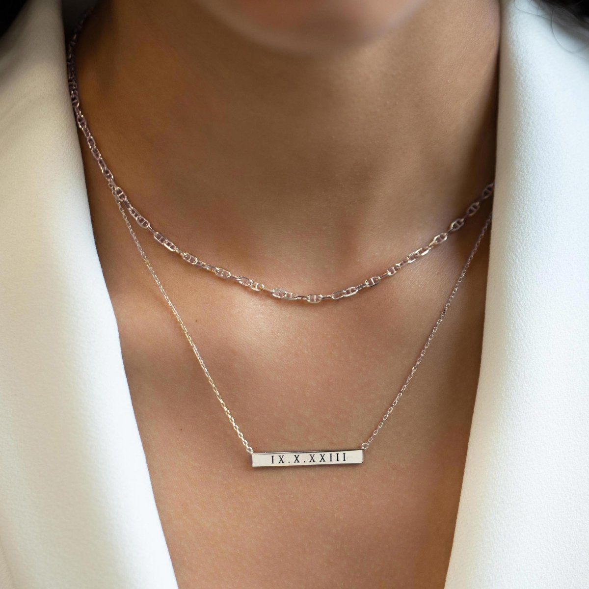 Sterling silver bar necklace engraved with a date, layered over a chain on a model's neckline