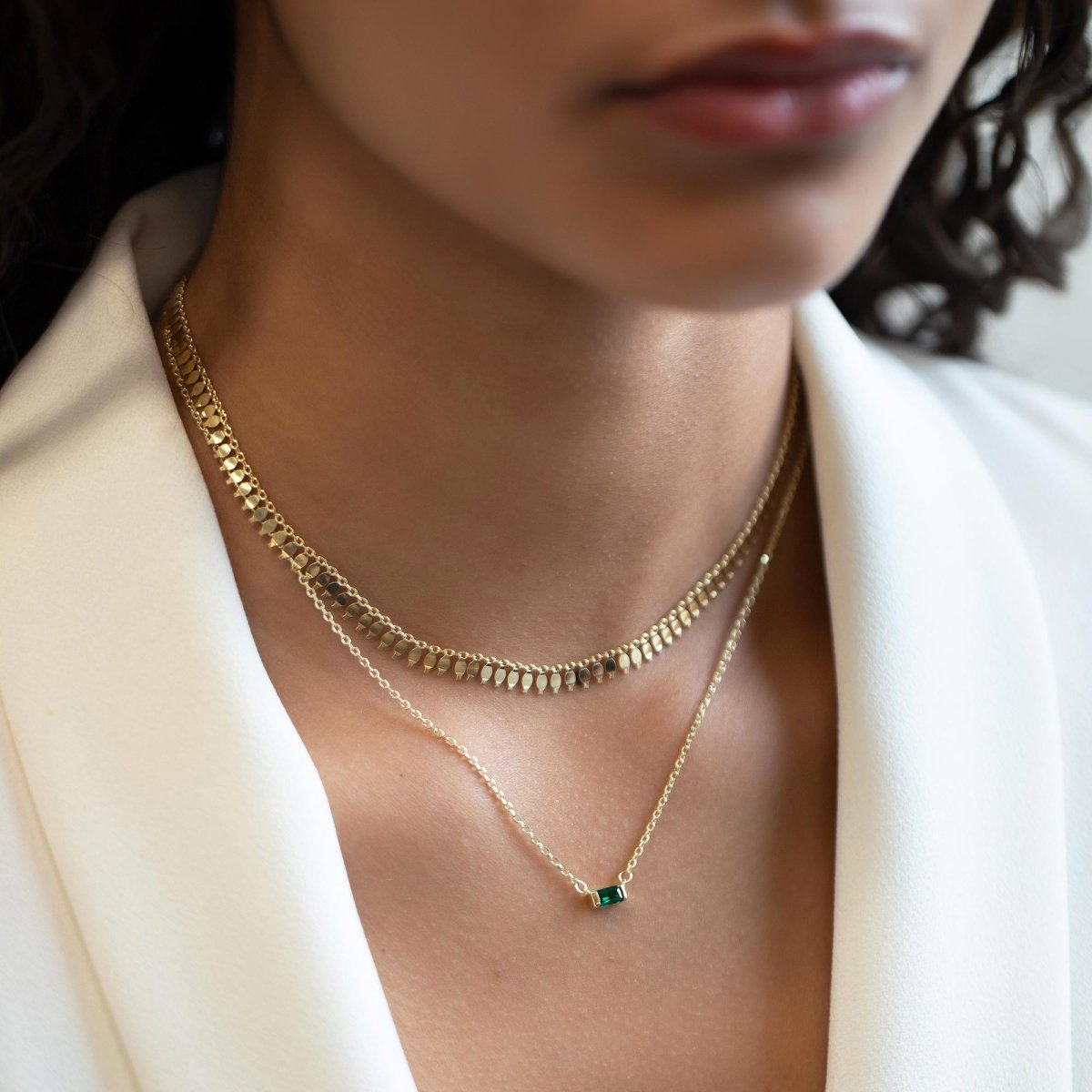 Gold vermeil emerald baguette necklace layered with a beaded chain, shown on a model's neckline
