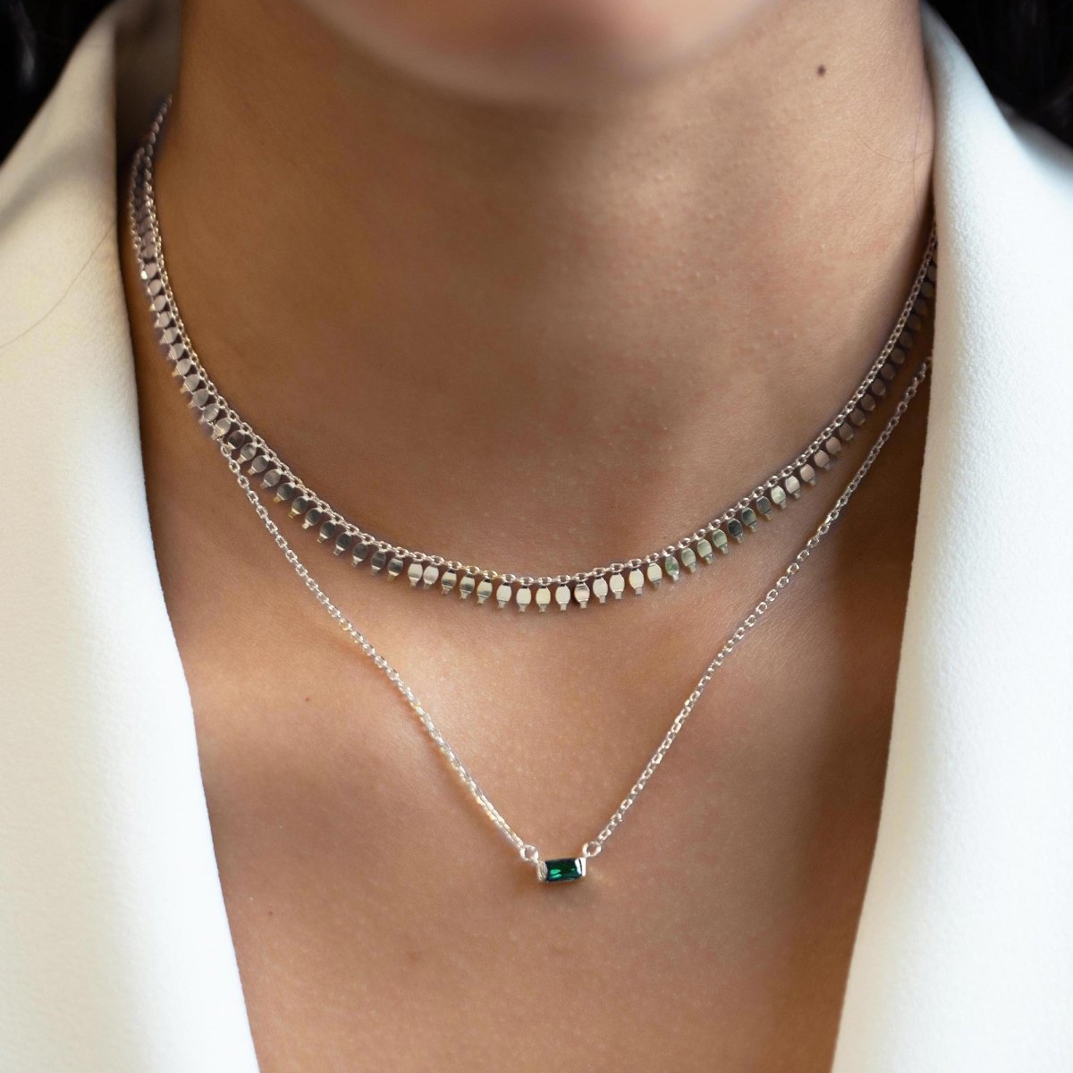 Sterling silver emerald baguette necklace layered with a beaded chain, shown on a model's neckline