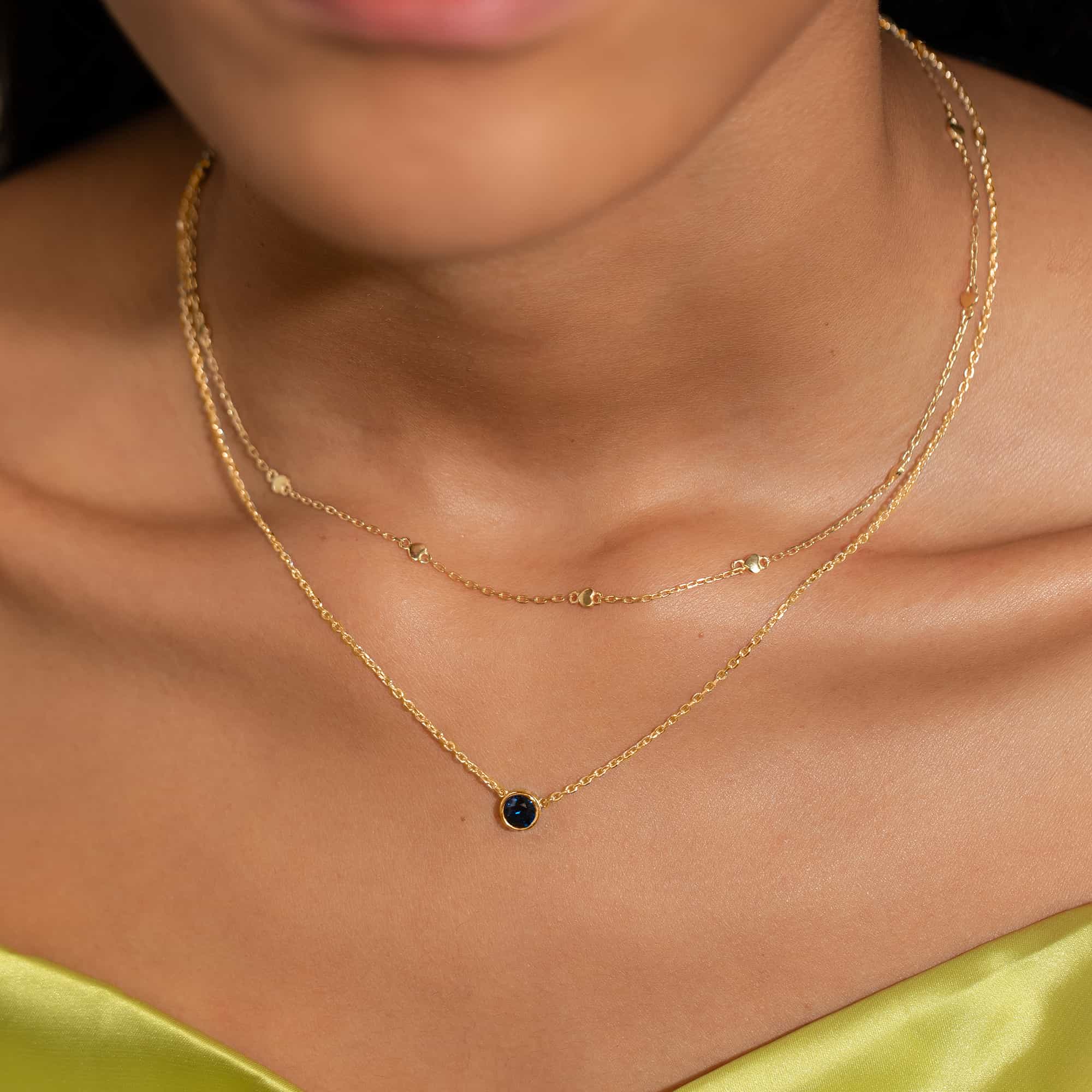 Gold vermeil solitaire necklace with a round blue sapphire pendant, shown layered on a model's neckline