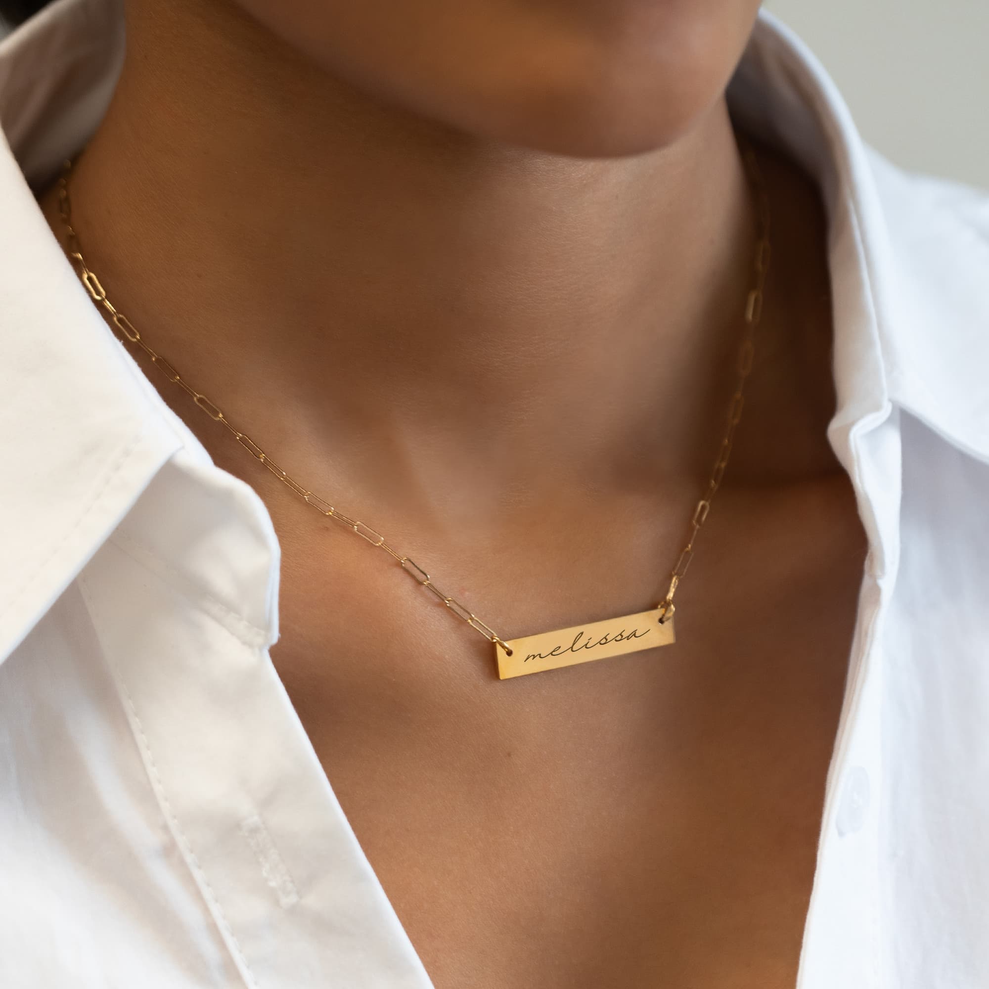 Gold-filled engravable bar necklace engraved with a name, shown on a model's neckline