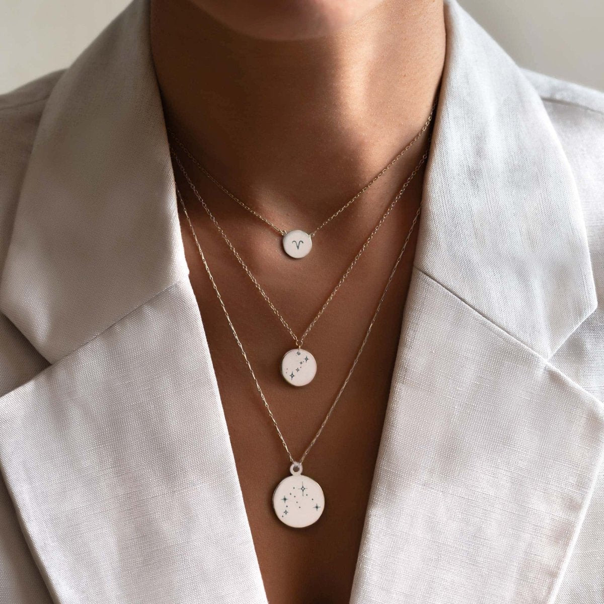 Sterling silver zodiac disc pendants layered at three lengths, shown on a model's neckline