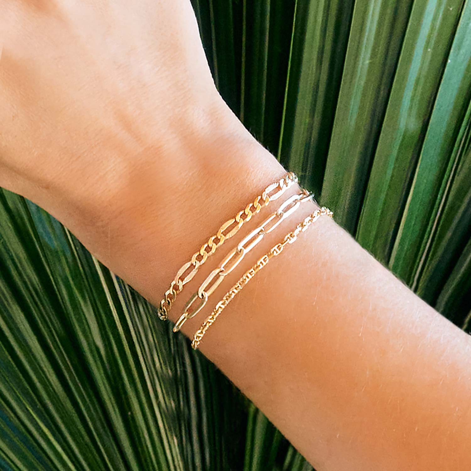 Gold vermeil faceted Figaro chain bracelet layered on a model's wrist against palm leaves