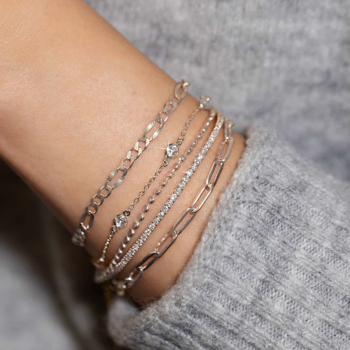 Sterling silver paperclip chain bracelet stacked with other silver chain bracelets on a wrist