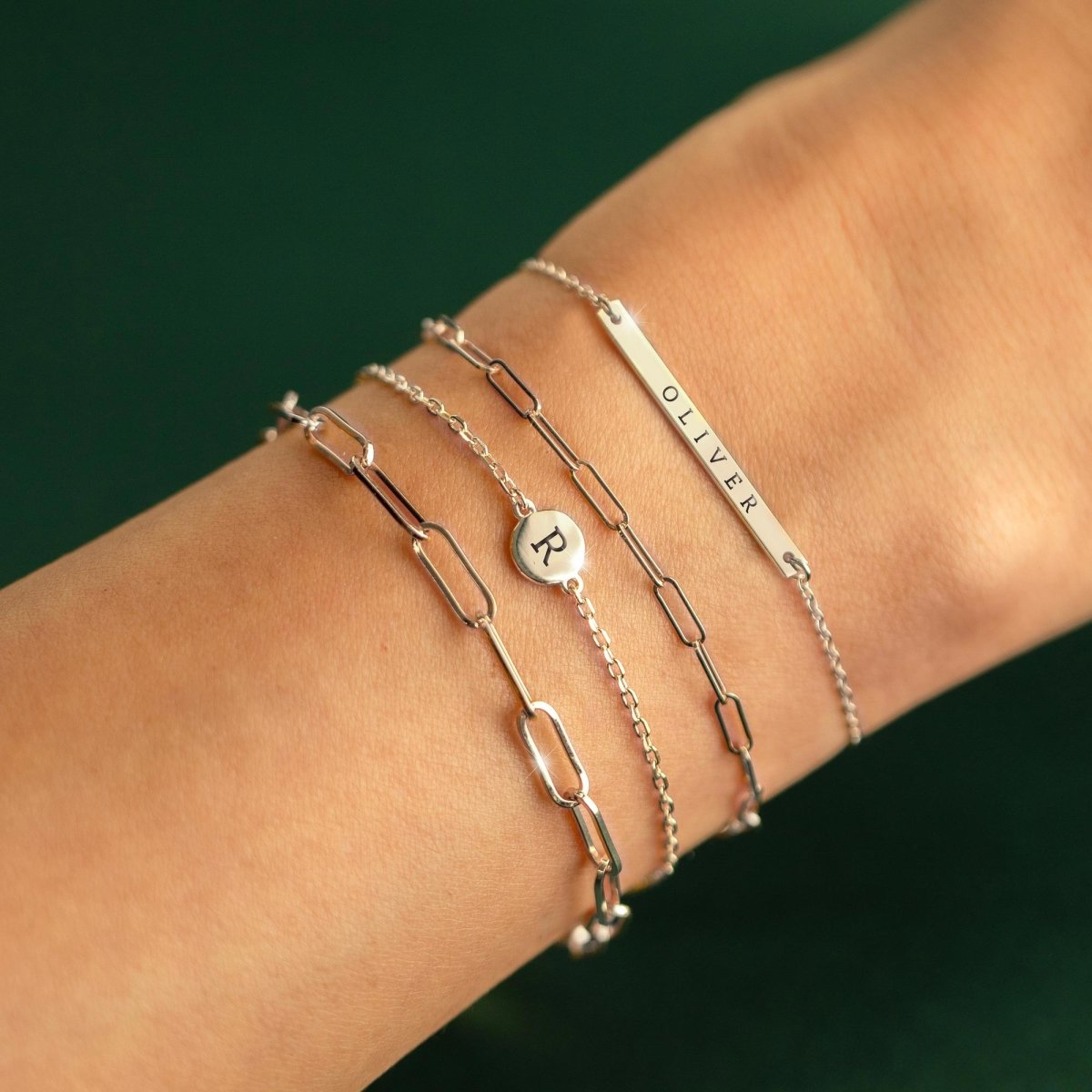 Sterling silver bracelet stack with an initial disc and a name-engraved bar, shown on a wrist