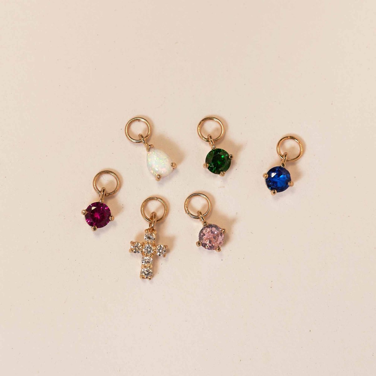 14K gold crystal cross charm with green, blue, pink, red, opal-white birthstone charms, on a cream background