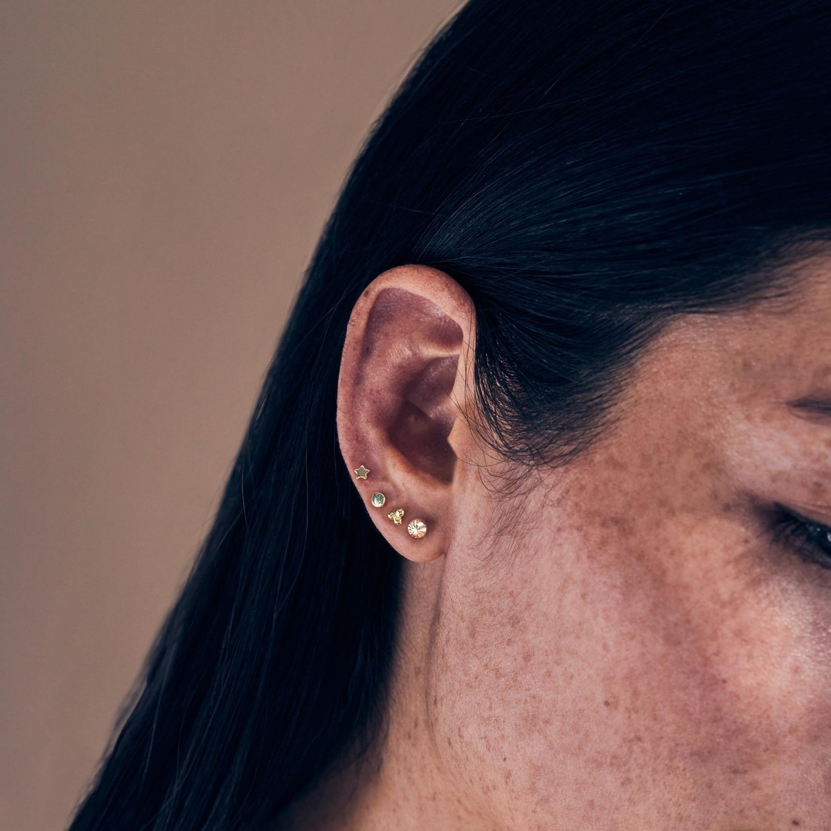 14K gold faceted ball stud earring shown on a model's lobe among other studs