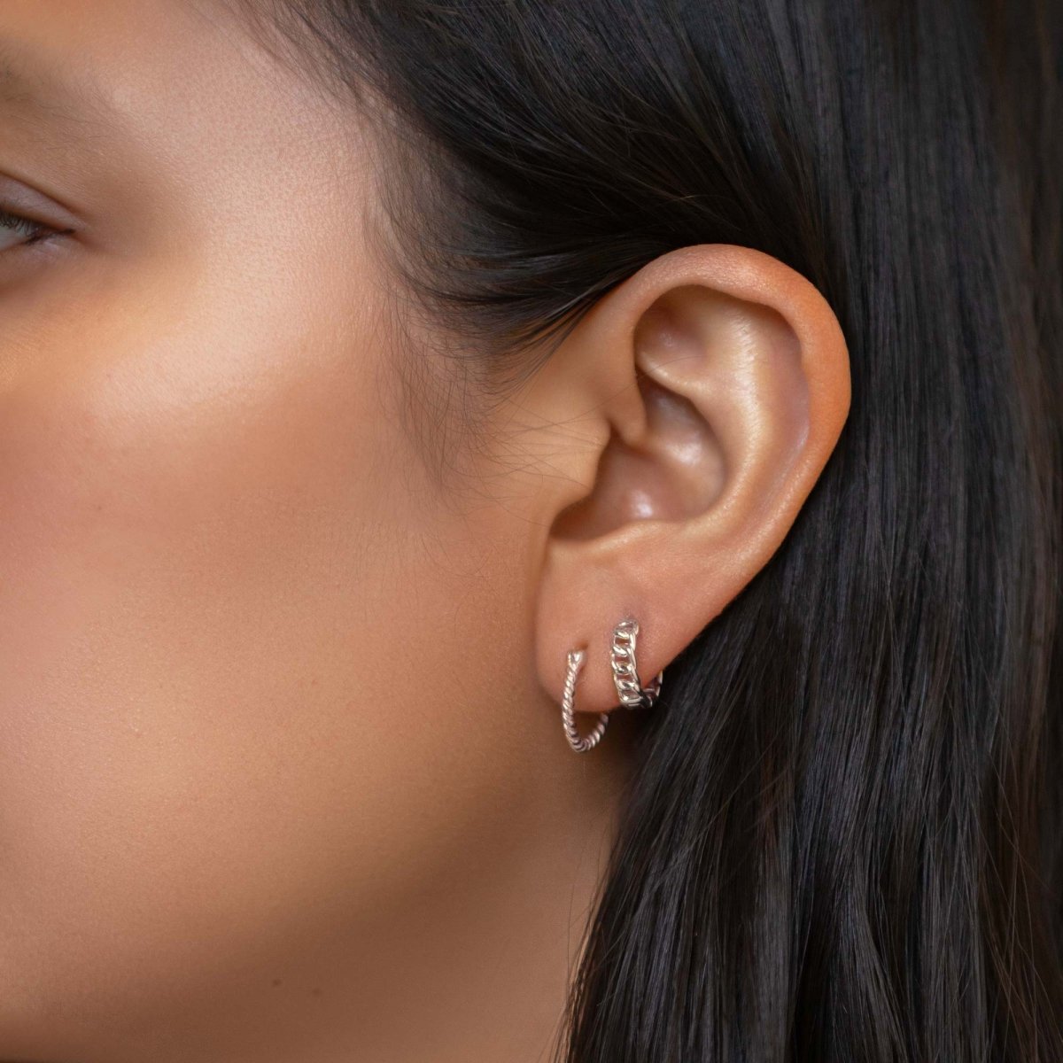 Sterling silver twisted rope huggie hoop stacked with a curb-chain hoop, on a model's lobe