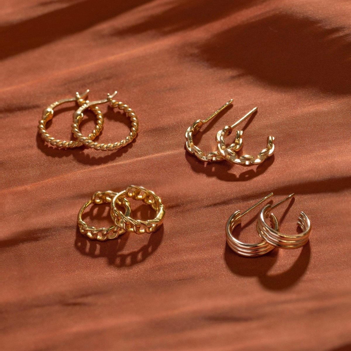 Gold-filled ridge hoops styled with twisted and curb-link hoops on a rust silk surface
