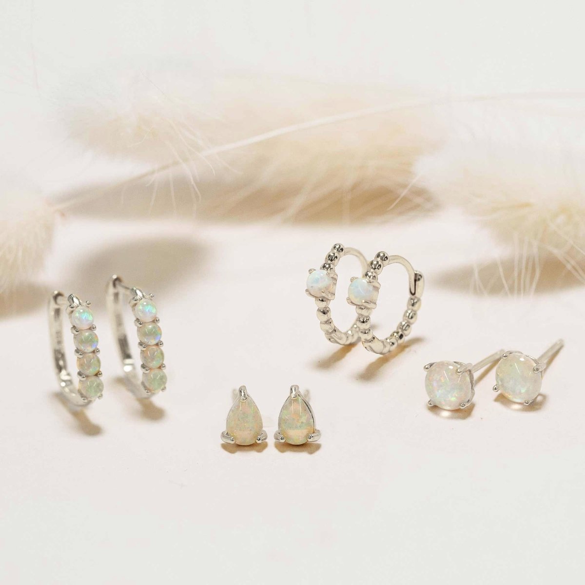 Sterling silver white opal earring set with huggies, pear studs and round studs, on a cream background