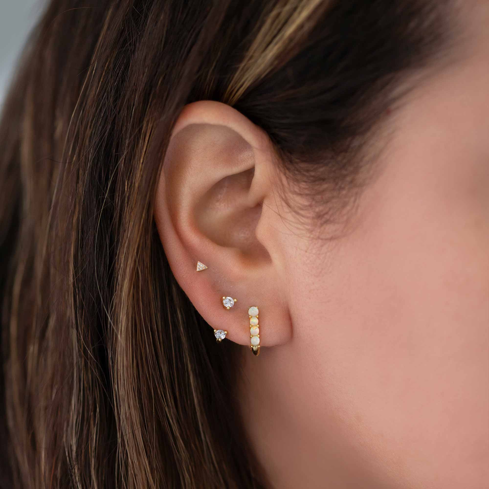 14K gold pavé triangle stud with clear stones, shown on a model's lobe above an opal-look huggie