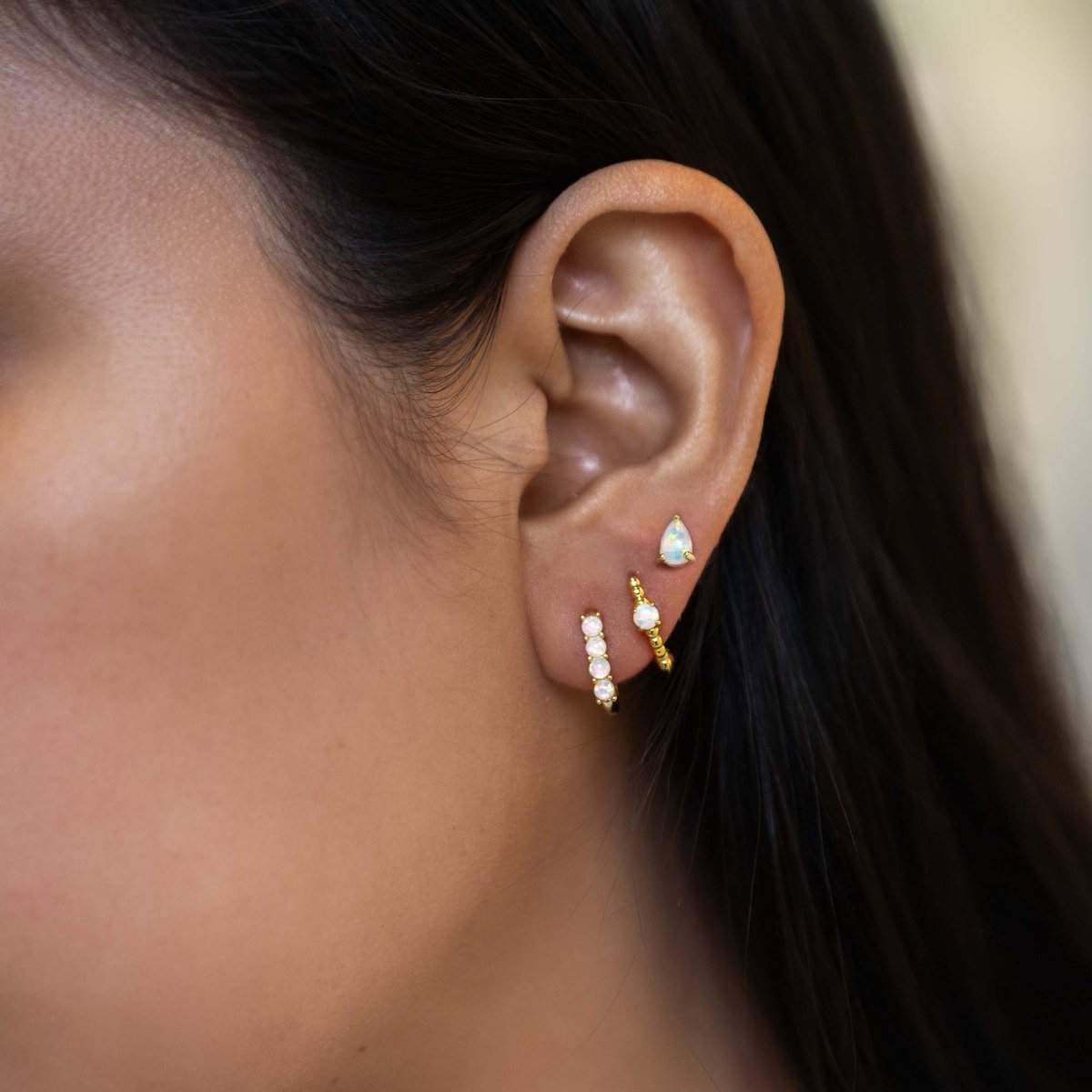 Gold vermeil white opal huggie hoops and pear stud shown stacked on a model's lobe and upper lobe