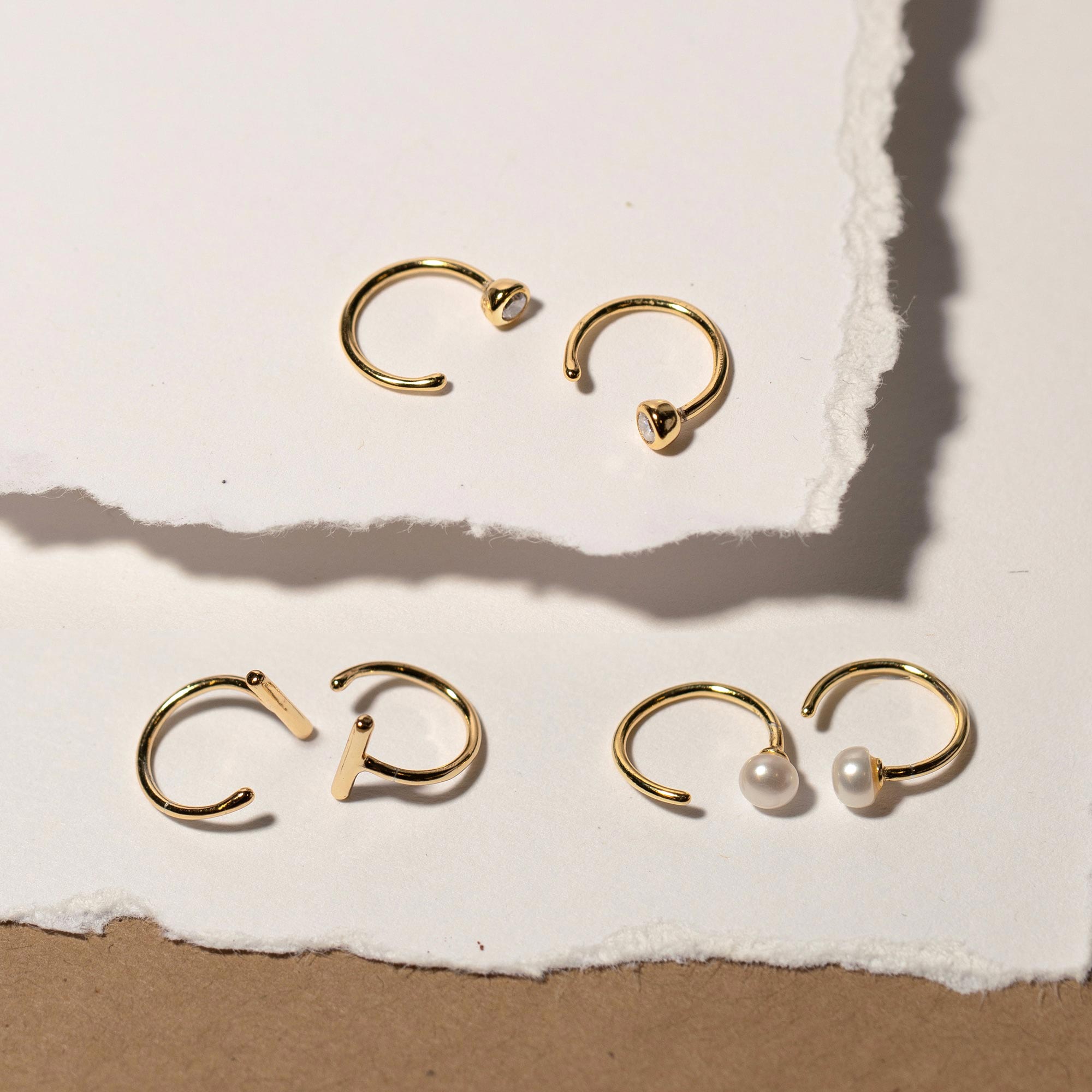 Gold vermeil open huggie hoops with white zirconia, shown with pearl and plain styles on paper