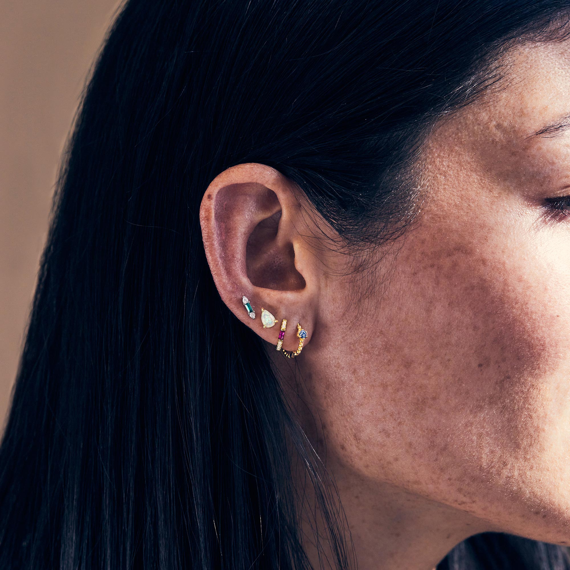 Close-up of woman's ear featuring Gold Vermeil gemstone Bead Huggies Gemstone Blue Zircon CZ Crystal paired with other gemstone earrings. 