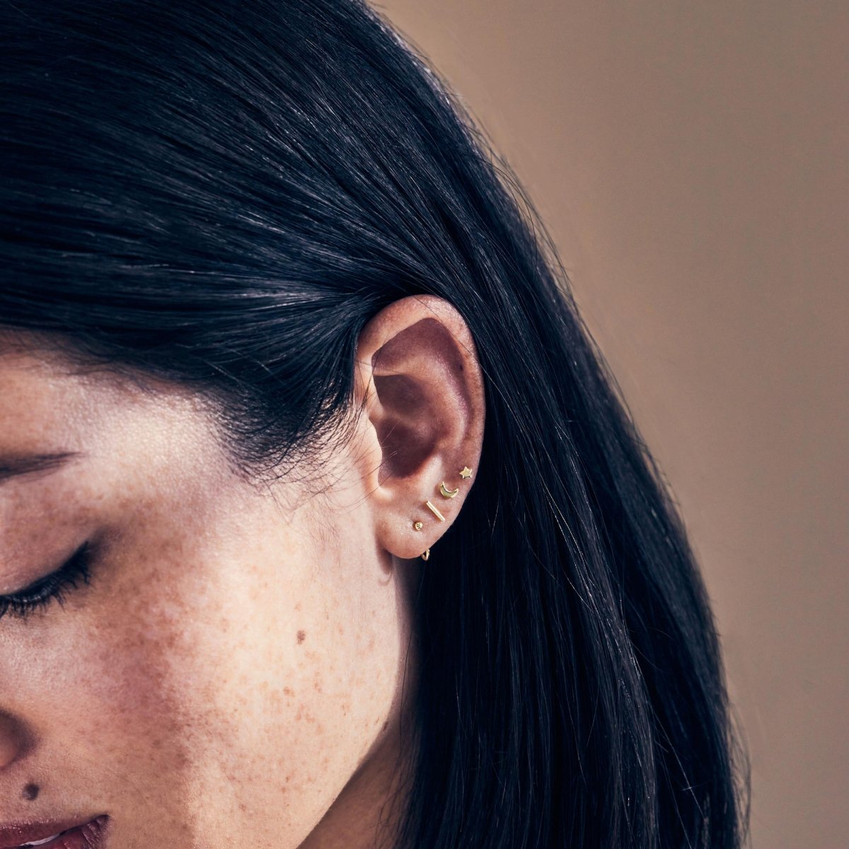 Gold vermeil thin bar stud shown on a model's upper ear in a stack of tiny studs
