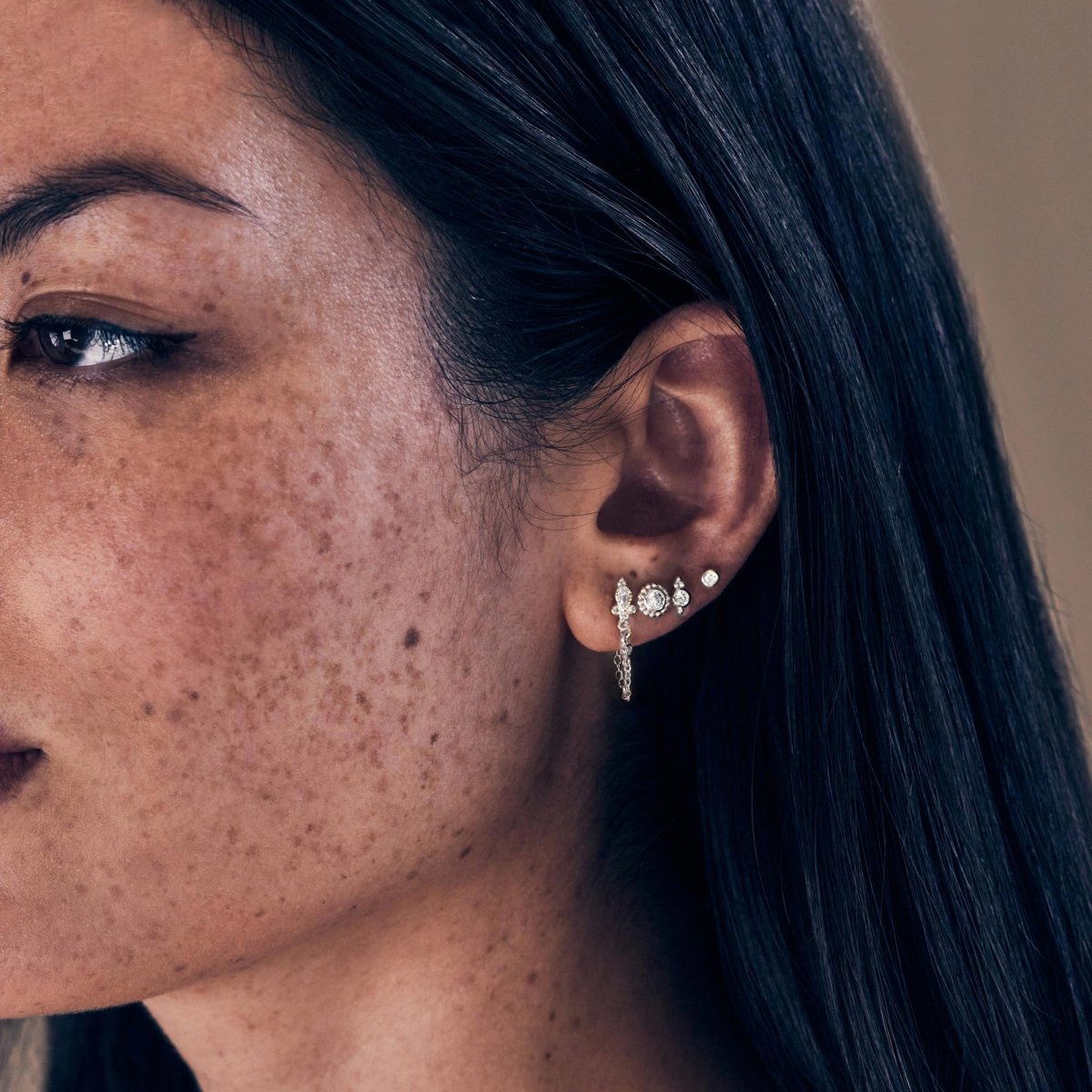 Sterling silver bezel zirconia stud worn on a model's lobe with a chain-drop stud in an ear stack