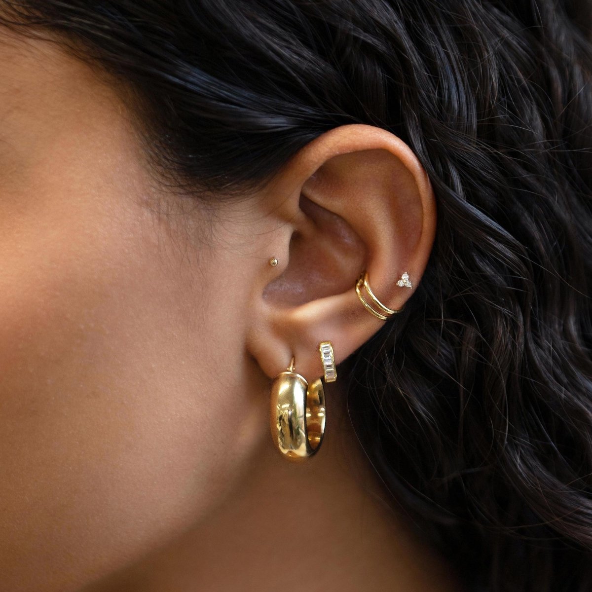 Close up of woman's ear featuring 14K Gold Tiny Clover Pave Stud paired with chunky gold hoops and ear cuff 