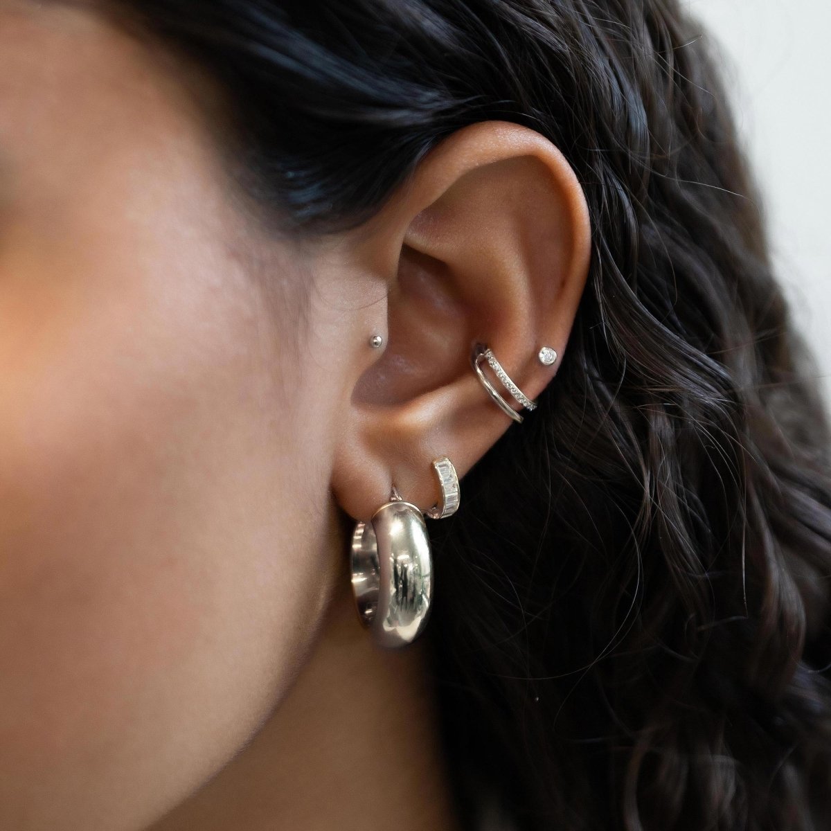 14K white gold baguette huggie hoop with clear stones, layered in an ear stack on a model