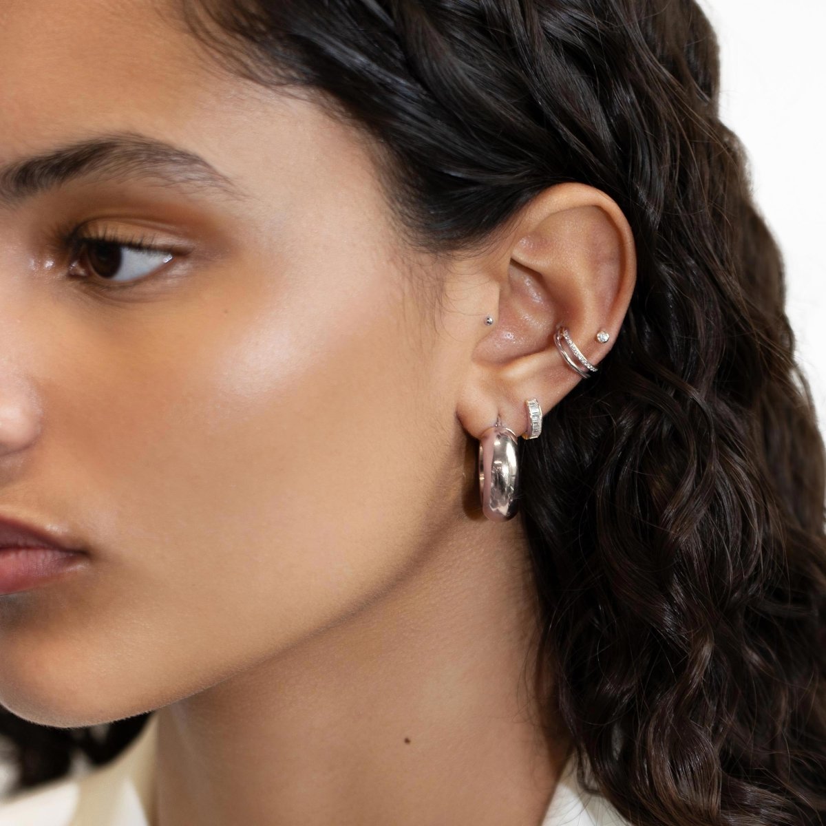 14K white gold baguette huggie hoop with clear stones, layered in an ear stack on a model