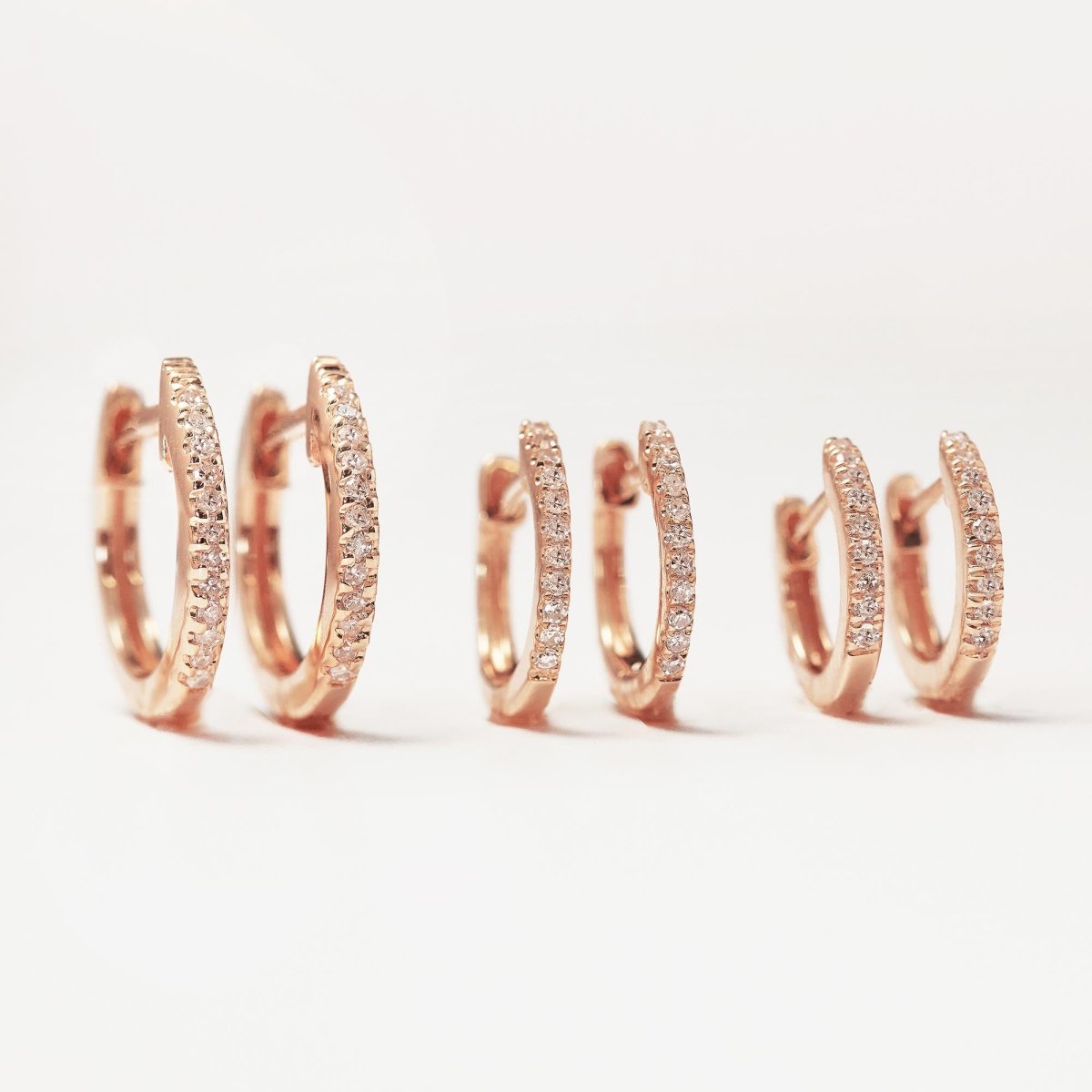 14K rose gold pavé diamond huggie hoops, close-up detail on cream fabric