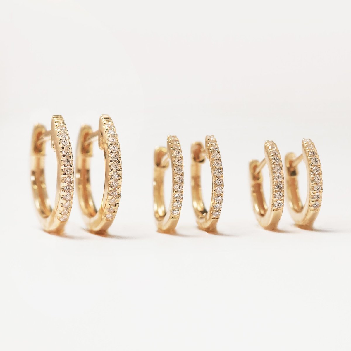 14K gold pavé diamond huggie hoops shown in three sizes, on a white background