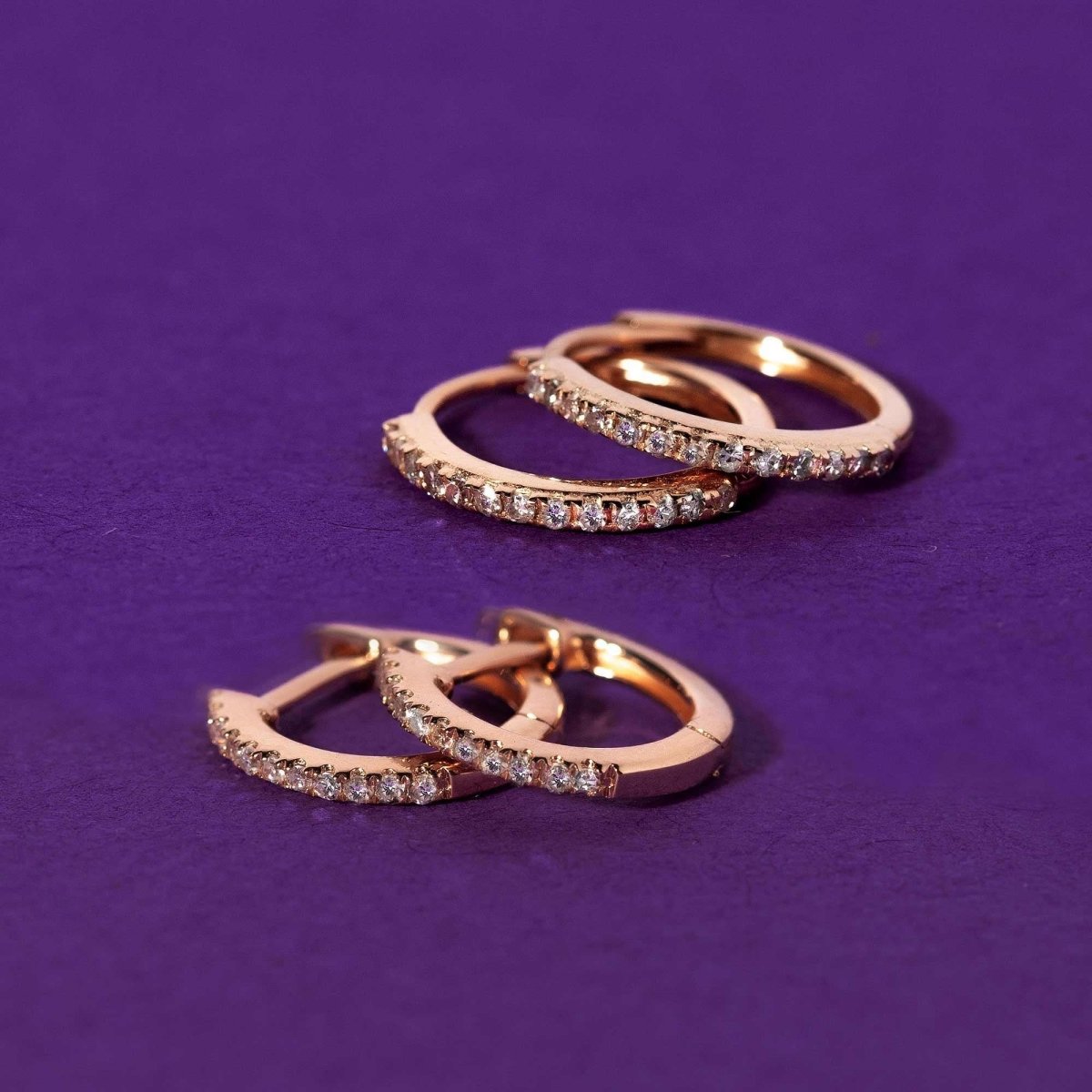 14K rose gold pave diamond huggie hoops, two sizes shown on a purple surface