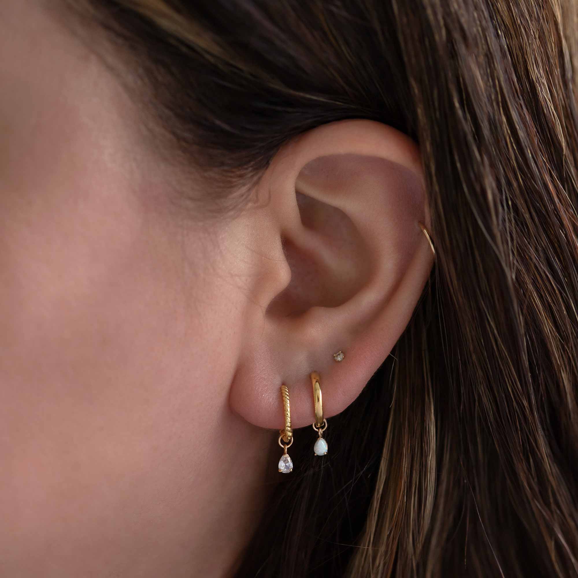 14K gold huggie hoops with pear clear-stone and white opal drop charms, close-up on a model's lobe