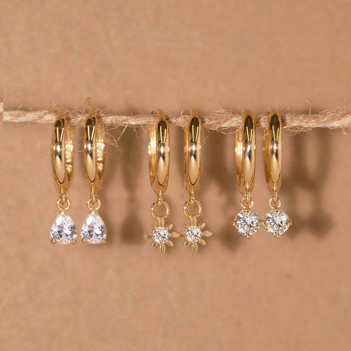 Three 14K gold huggie hoops with teardrop, starburst, and round zirconia charms, on a string