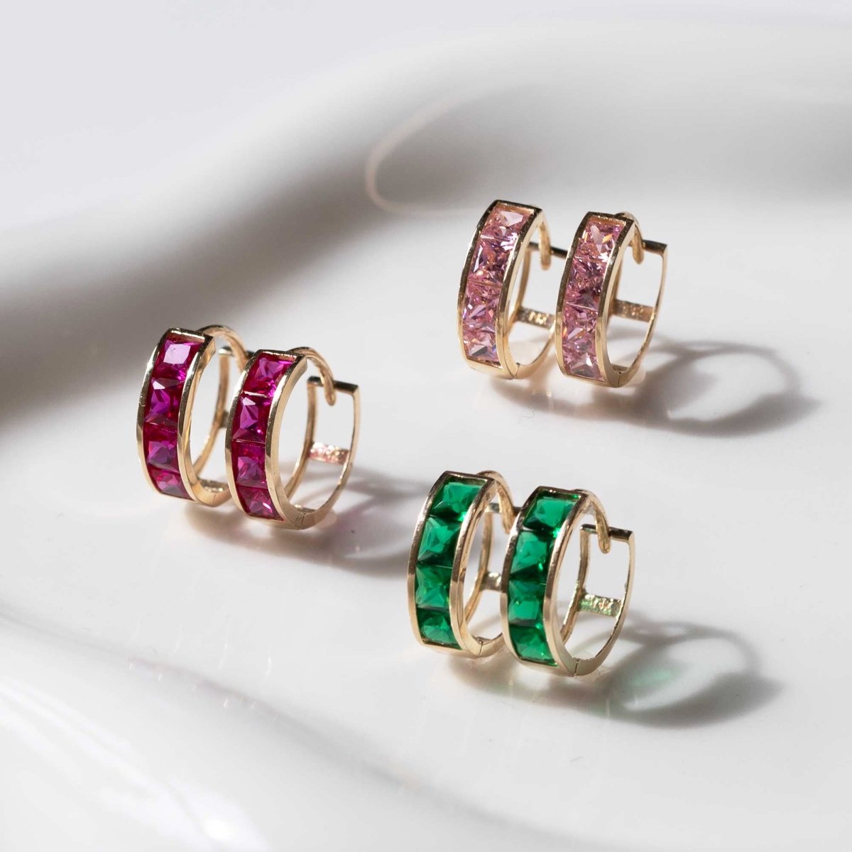 14K gold ruby, pink sapphire and emerald huggie hoops grouped on a white tray