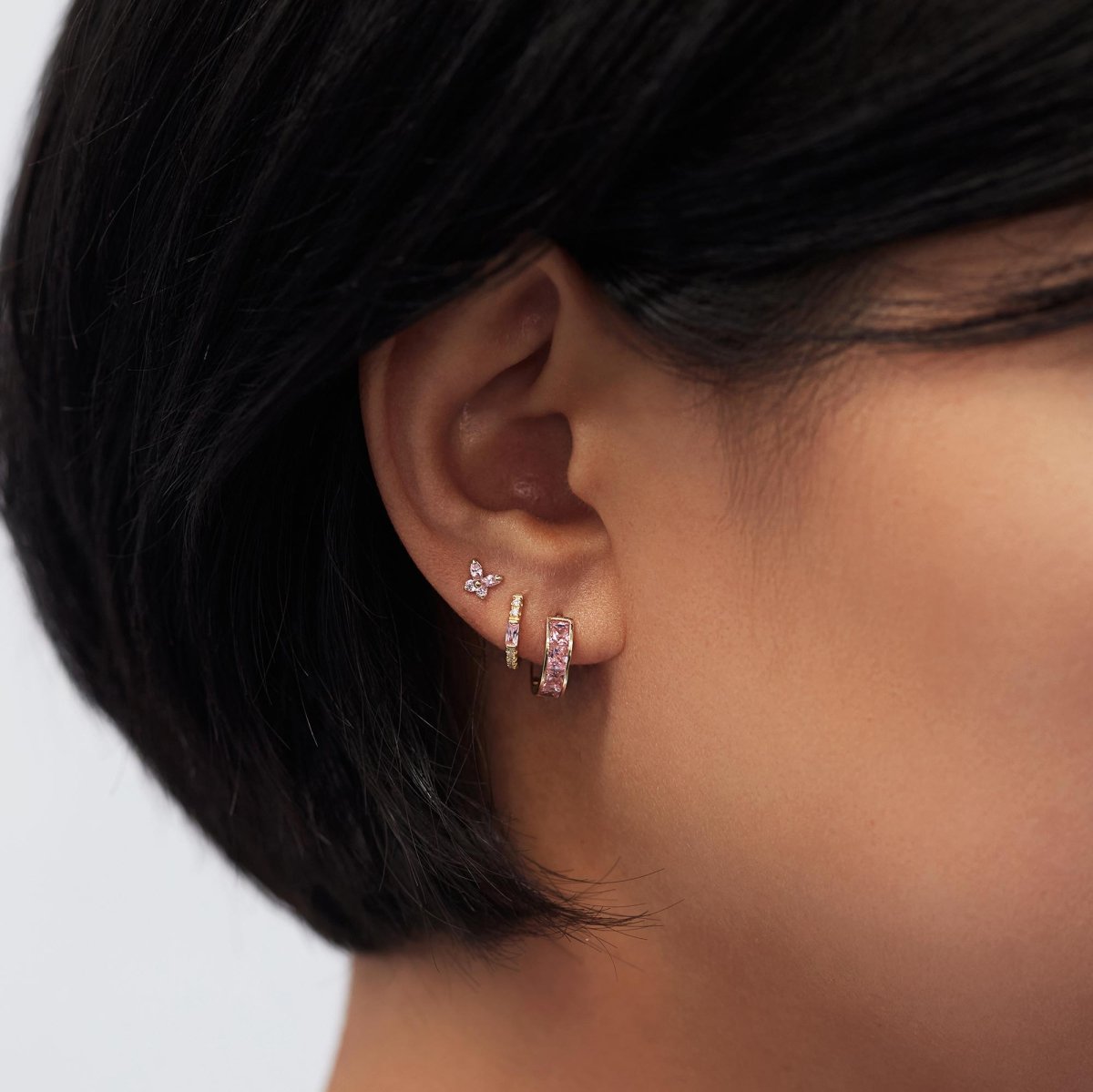 Gold vermeil pink sapphire baguette huggie hoop, shown on a model's lobe in a stack with pink studs