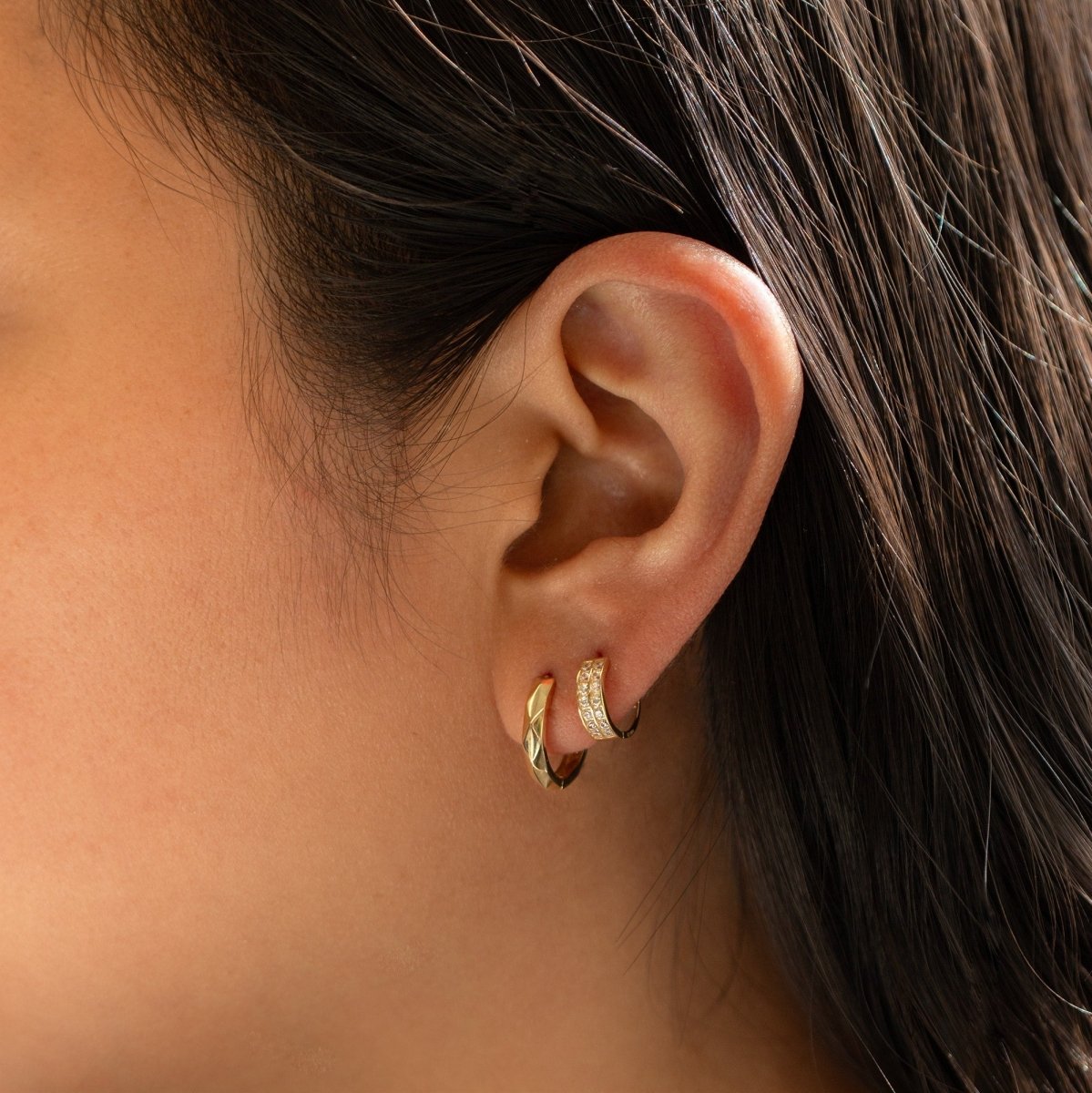 14K gold faceted mini huggie hoop shown on a model's lobe with a pavé huggie