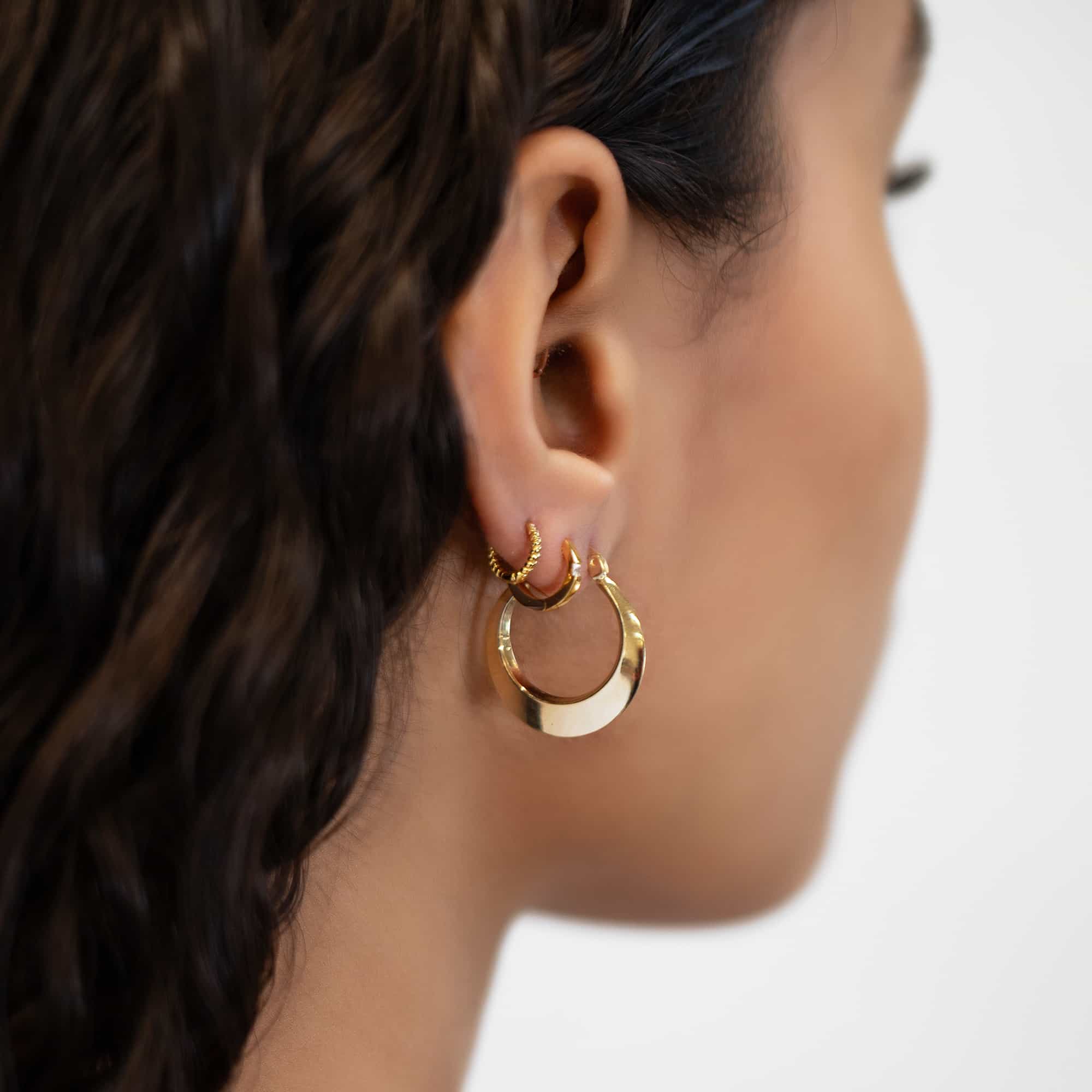 14K gold thin beveled-edge hoop earring, close-up detail on a model's lobe in an ear stack