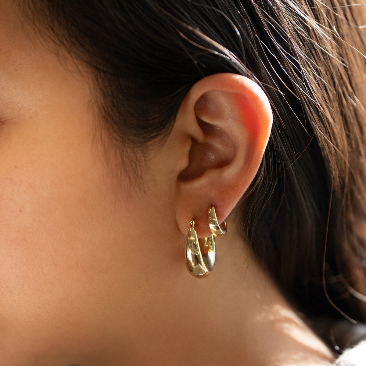 14K gold teardrop huggie hoops shown stacked on a model's lobe